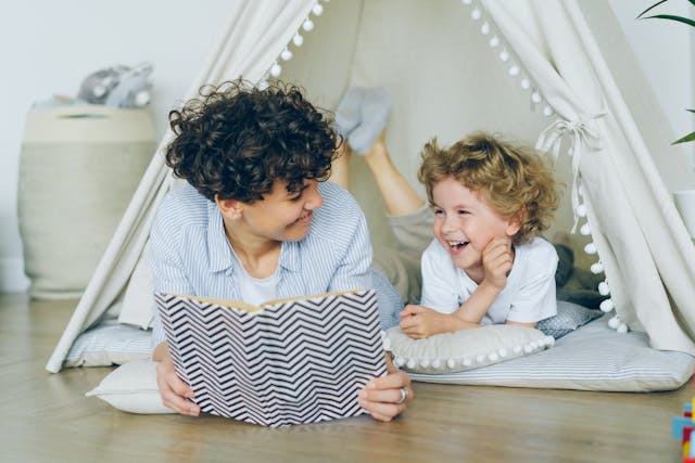 A joyful mother and son enjoying reading together in a cozy indoor tent setting.